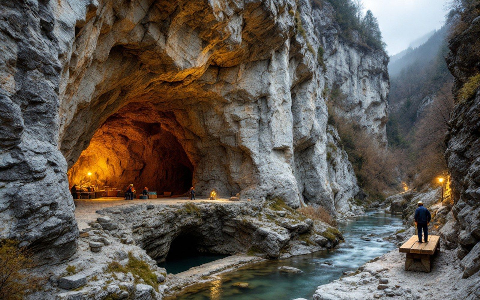 A limestone cliff face above a river with a cave opening at its base